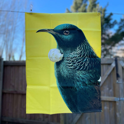 Bright yellow tea towel with a Tui on it.